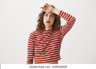 So much work left. Studio shot of emotive and funny woman in stylish outfit wiping of sweat from forehead and sulking, frowning while looking at camera with tired and bothered expression.