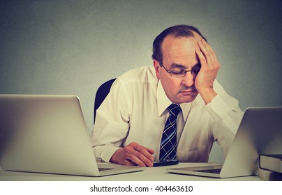 Too Much Work Tired Sleepy Middle Aged Man Sitting At His Desk With Books In Front Of Two Laptop Computers Isolated On Grey Wall Office Background. Busy Schedule In College Workplace Sleep Deprivation