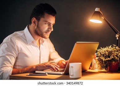 So Much Work Today! Confident Young Man Working On His Laptop While Sitting At His Working Place At Night Time