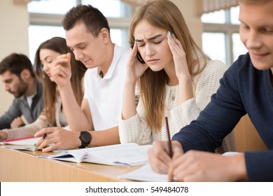 Too much work. Young attractive female student suffering from headache from overworking in school university college stress stressed exhausted tired pain headache migraine students sitting in a row