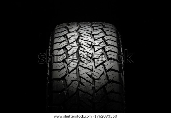 mud all-season all terrain tire\
with a powerful tread. Front view on a black background close\
up