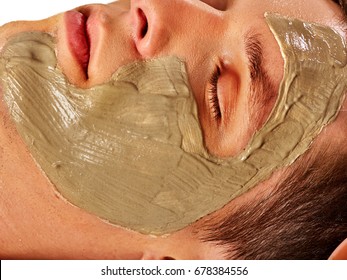 Mud facial mask of man in spa salon. Massage with clay full face. Close up man lying on spa bed on therapeutic procedure . Cropped shot of home cosmetics with egg yolk.