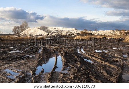 Mud and puddles on the dirt road with sand hills in the background.