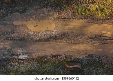 Mud and puddles seen from above, rough muddy terrain with visible tire marks imprinted in the surface