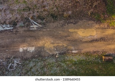 Mud and puddles seen from above, rough muddy terrain with visible tire marks imprinted in the surface