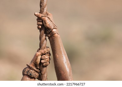 Mud race runner. Detail of muddy hands they climb the rope. Athletic man working out and climbing a rope, during obstacle course - Powered by Shutterstock