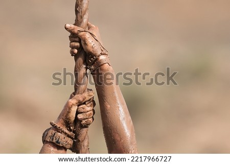 Mud race runner. Detail of muddy hands they climb the rope. Athletic man working out and climbing a rope, during obstacle course