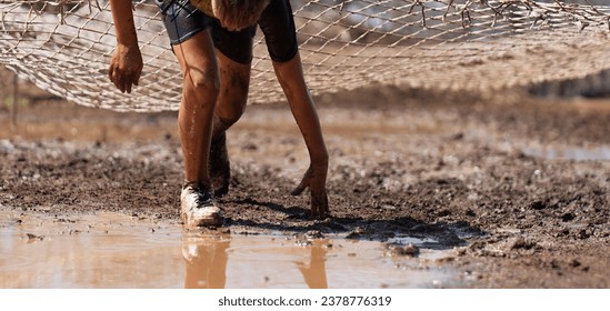 Mud race runners. Crawling, passing under a net obstacle during extreme obstacle race - Powered by Shutterstock