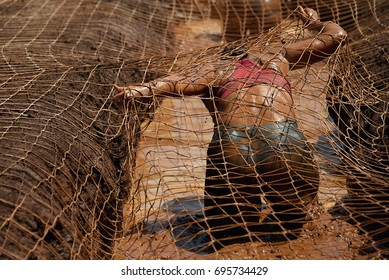 Mud Race Runners.Woman Covered With Mud Fighting To Get Out Of A Net In The Obstacle Race