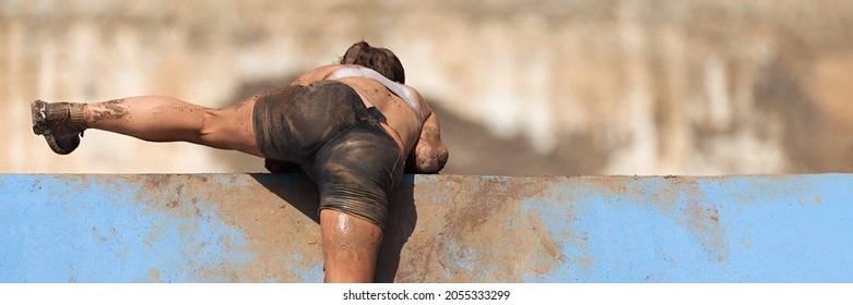 Mud Race Running. Running Over Obstacles Female Race Participant, Climbs Over Wall On Obstacle Course