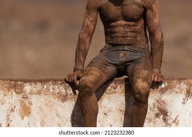 Mud Race Running. Running Over Obstacles Male Race Participant, Climbs Over Wall On Obstacle Course