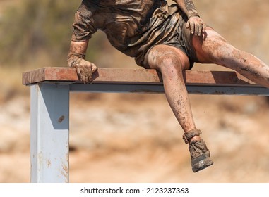 Mud Race Running. Running Over Obstacles Male Race Participant, Climbs Over Wall On Obstacle Course