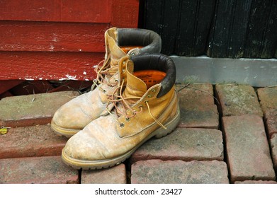 Mud-caked workboots on the brick walkway outside the black door to a bright red shed..