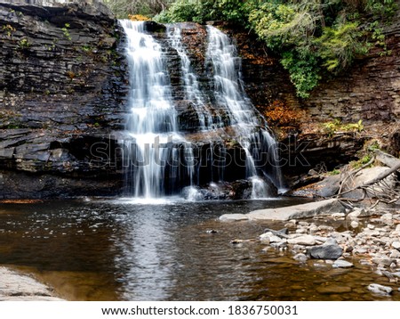 Muddy Falls in Swallow Falls State Park in Oakland, Maryland, the waterfall cascading and flowing down the side of the rocks in the autumn with leaves fallen in the water below.