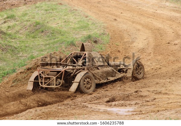 Muddy kartcross buggy car on turn\
off road dirt track, rear side view on speed autocross\
racing