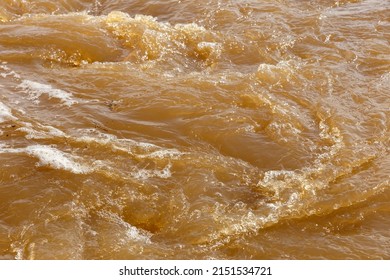 Muddy river water. Dirty muddy water with whirlpool and white foam close-up.