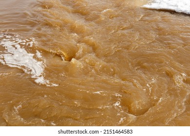 Muddy river water. Spring flood. Dirty muddy water with whirlpool and white foam close-up.