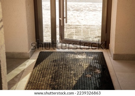 Muddy rubber doormat mounted on tiled floor inside of house entrance in winter time. Cleaning service and household concept.