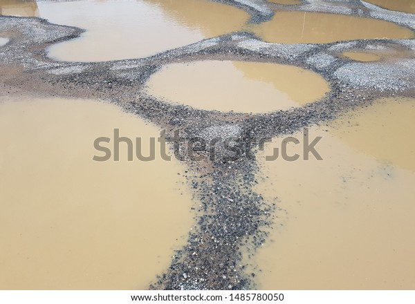Muddy water in the big\
holes of road after rain. Cracked cement road. Transportation\'s\
problem concept.