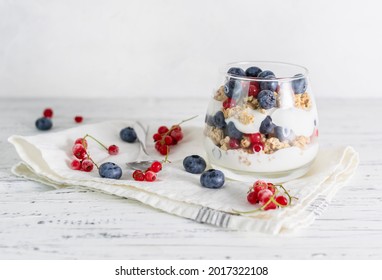 Muesli with blueberries, red currants and sour cream in a transparent glass. Sprigs of red currant and blueberry on a light napkin - Powered by Shutterstock