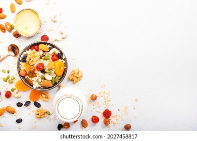 Muesli bowl and ingredients for healthy breakfast. Granola, nuts, dried fruits, flakes, honey and greek yogurt on white table copy space