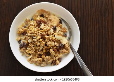 Muesli Fruit And Fiber Cereal With Dry Oat, Corn, Banana, Raisin, And Apple With Milk On A White Bowl. Flat Lay Top View Photo. Copy Space Is On The Right Side.