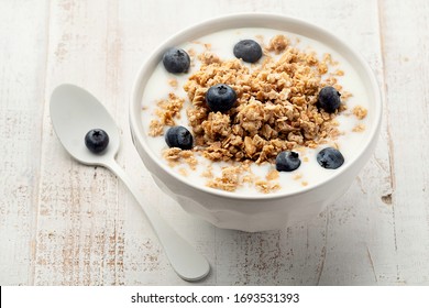 Muesli with yoghurt in a bowl on white wooden background