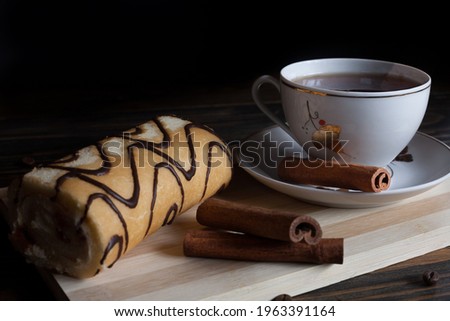 A mug of aromatic black coffee in a white cup with dessert, coffee beans and cinnamon sticks, on a wooden background. Coffee break. 