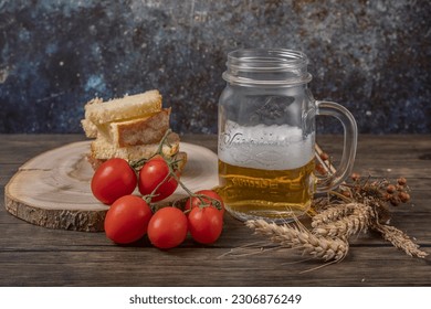 A mug of beer with toasted bread and red cherry tomatoes next to it, with dried ears of corn - Powered by Shutterstock