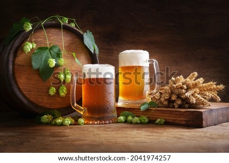 mug of beer, wheat ears, green hops and beer barrel on a wooden background