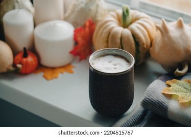 Mug Of Coffee Standing Next To The Window With Candles, Pumpkins, Book And Warm Blanket. Cozy Home Atmosphere In Sunny Autumn Day. Cozy Fall Composition.