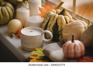 Mug Of Coffee Standing Next To The Window With Candles, Pumpkins, Book And Warm Blanket. Cozy Home Atmosphere In Sunny Autumn Day. Cozy Fall Composition.