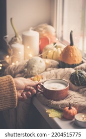 Mug Of Coffee Standing Next To The Window With Candles, Pumpkins, Book And Warm Blanket. Cozy Home Atmosphere In Sunny Autumn Day. Cozy Fall Composition.