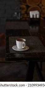 A Mug Of Coffee Stands On A Tray In A Restaurant.  Dark Colors, Loft Style Interior.  No People