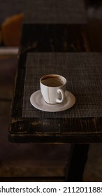 A Mug Of Coffee Stands On A Tray In A Restaurant.  Dark Colors, Loft Style Interior.  No People