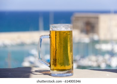 Mug of cold beer on the background of the sea and pier with yachts