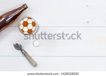 Mug of craft beer with a soccer ball on a beer foam and bottle with retro opener on light wooden background. Top view. Empty space for text