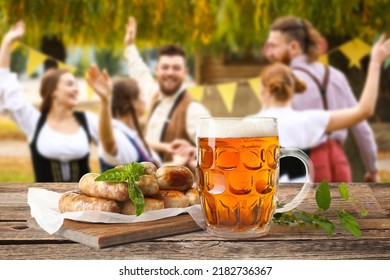 Mug of fresh beer and sausages on table outdoors. Oktoberfest celebration