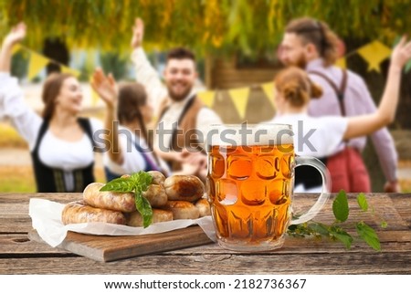 Mug of fresh beer and sausages on table outdoors. Oktoberfest celebration