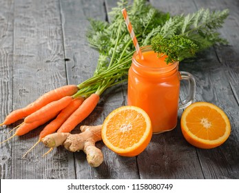 A mug of fresh carrot smoothie with cocktail straw, parsley, ginger root and oranges on a dark wooden table. The concept of healthy eating.
