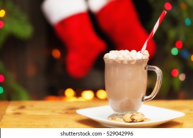 Mug of hot chocolate with marshmallows on a plate with cookies in front of decorated fireplace - Powered by Shutterstock