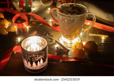 A mug of hot chocolate with whipped cream on top and a candy cane standing on a wooden rustic table with a winter themed burning candle, traditional spices, satsumas  and tangerines and fairy lights - Powered by Shutterstock