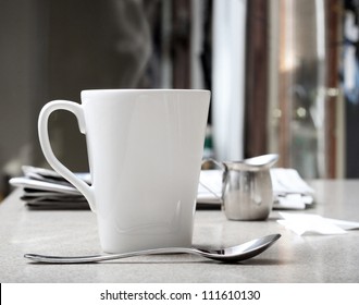 Mug Of Hot Coffee Or Tea With Stainless Creamer And Morning Newspaper On Counter. Intentionally Desaturated For Effect