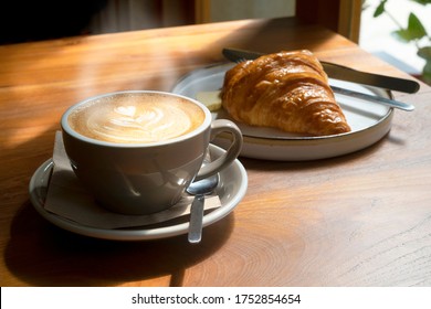 A mug of latte coffee with Croissant coffee break on wooden table, smoke on coffee 
