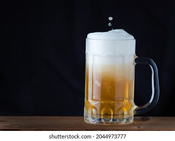 Mug of light beer pills with foam on a wooden table in a pub