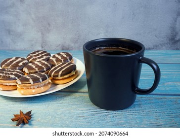 A Mug Of Natural Coffee Stands On A Blue Wooden Table Next To A White Plate With Chocolate Cookies. Side View