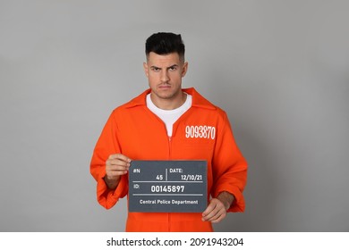 Mug Shot Of Prisoner In Orange Jumpsuit With Board On Grey Background, Front View