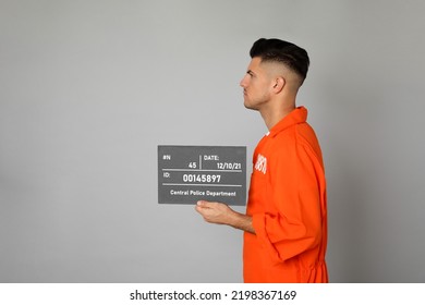 Mug Shot Of Prisoner In Orange Uniform With Board On Grey Background, Side View