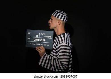 Mug Shot Of Prisoner In Striped Uniform With Board On Black Background, Side View