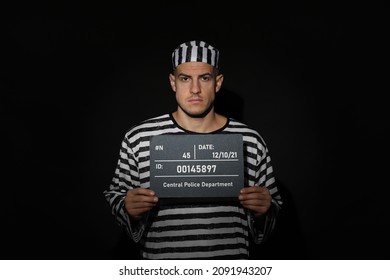 Mug Shot Of Prisoner In Striped Uniform With Board On Black Background, Front View